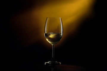 White wine in a glass on a gradient black to yellow background. Studio shot.