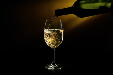 White wine being poured in a wine glass on a dark background. Studio close-up shot.