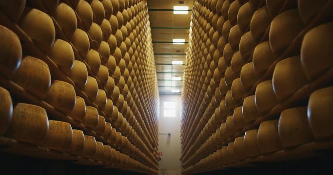 Slow motion slider view of lots of wheels of parmesan cheese are maturing by ancient Italian tradition for many months on shelves of a storehouse.