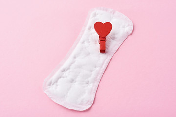 Sanitary pad and red wooden heart on a pink background