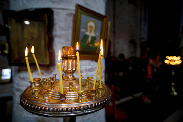 Round candlestick with burning candles in the interior of russian orthodox church. Candles under the ancient icon framed with the gold. Сelebration of holy holidays