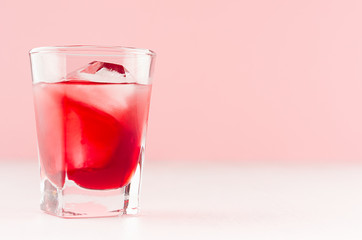 Elegant sweet red strawberry alcoholic cocktail with ice cubes in shot glass in soft light pink bar interior, copy space.