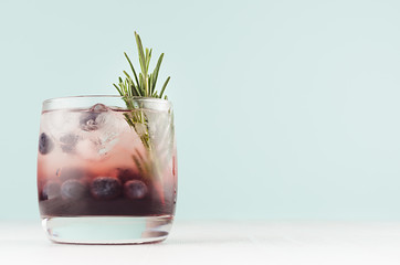 Fresh summer juicy cocktail in glass with ice cubes, blueberry, rosemary in modern youth interior...