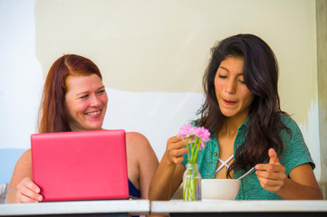 young happy caucasian woman and beautiful hispanic girl working at office cafe with laptop computer discussing as digital business partners and diversity ethnicity friends