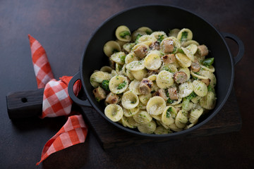 Orecchiette with broccoli sauce, chopped pork sausages and grated parmesan in a cast-iron stewpan over dark brown metal background