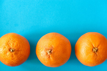 Closeup of a horizontal row of three vibrant orange blood oranges on light blue or teal background with copy space. Flat lay