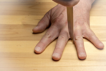 Dangerous game. Blade of the knife between the fingers on the background of a wooden table