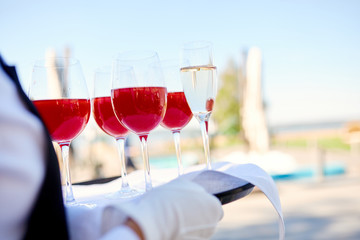 four wine glasses with red alcoholic drink and one glass of champagne on a tray of the waiter