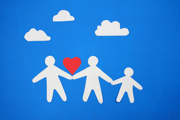 Paper figures of mom, dad and baby holding hands on a blue background. The concept of a happy family.