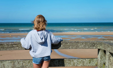 Back view of young happy teenage girl stands on old pier and looks at the ocean landscape.