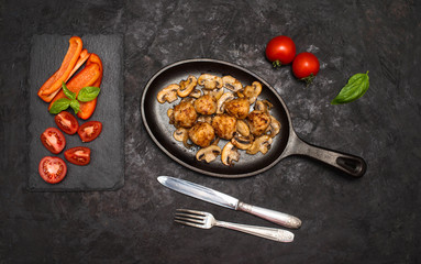 Delicious homemade meatballs served with mushrooms on iron cast pan and fresh vegetables. Top view.