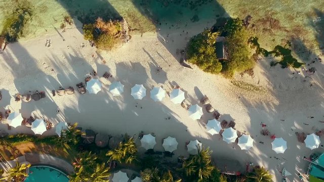 Video loop with aerial footage showing bird eye view with people walking and getting tan on a tropical Florida beach under blue umbrellas and turquoise ocean waves breaking against the coastal line