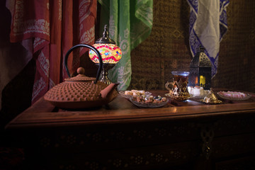 Arabian tea in glass with eastern snacks on vintage wooden surface. Eastern tea concept. Low light lounge interior with carpet. Empty space.