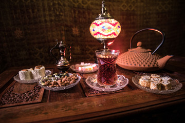 Arabian tea in glass with eastern snacks on vintage wooden surface. Eastern tea concept. Low light lounge interior with carpet. Empty space.