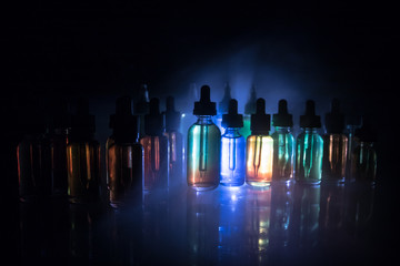 Vape concept. Smoke clouds and vape liquid bottles on dark background. Light effects. Useful as...