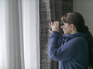 Young woman watching through binoculars through the window