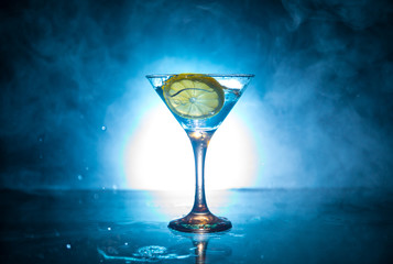 Martini cocktail glass in hand splashing on dark toned smoky background or colorful cocktail in glass with splashes and olives. Party club entertainment. Mixed light. Selective focus