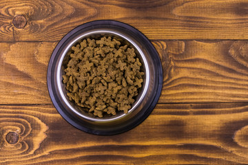 Dry cat food in bowl on wooden background. Pet food on wood surface. Top view