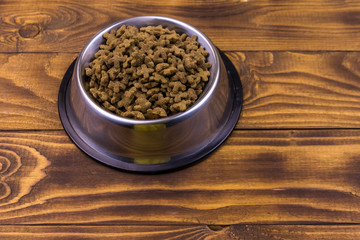 Dry cat food in bowl on wooden background. Pet food on wood surface