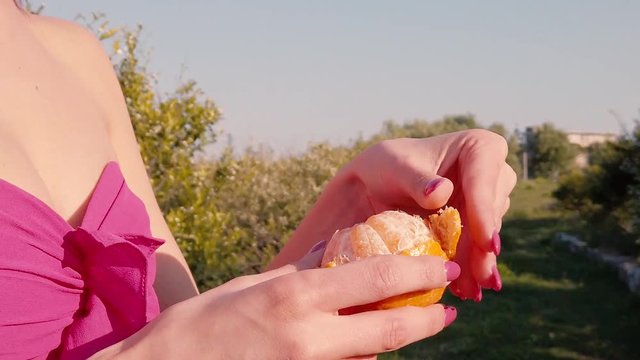 Mani di una ragazza vegetariana sta sbucciando un'arancia fresca presa dall'albero in campagna.