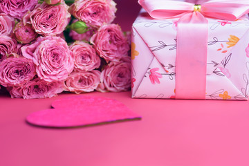 A bouquet of roses and a gift on a pink background