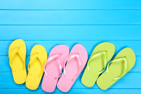 Pairs of colorful flip flops on blue wooden table