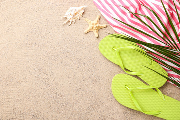 Fototapeta na wymiar Pair of flip flops with starfish and palm leaf on beach sand