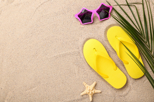 Pair of flip flops with starfish and palm leaf on beach sand