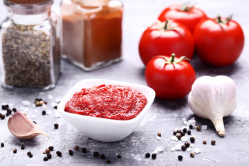 Ketchup in bowl with spices and garlic on grey wooden table