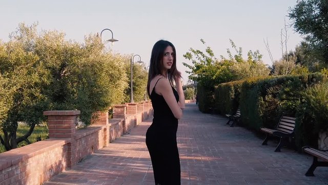 Super bella modella ricca e lussuosa con vestito nero e tacchi a spillo, cammina e fa il follow me alla telecamera. Ripresa di spalle al rallentatore.