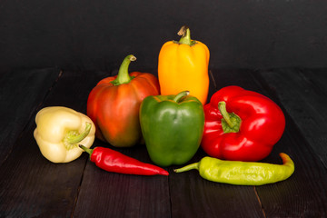 A composition of fresh peppers on a wooden black table. Tasty colored vegetables on a dark background. 