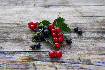 Fresh berries on a gray wooden table. Red and black currant with green leaves. Delicious vitamins in nature. 