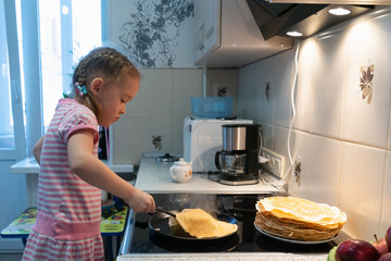 a little girl in a pink dress is frying pancakes on an electric stove