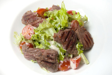 Veal salad, salad with large slices of veal and fresh vegetables on a plate on a black background.