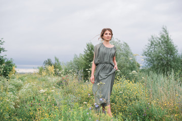 Naklejka na ściany i meble beautiful young girl in a summer dress in a field on a background of green grass