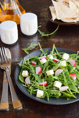 Salad of fresh vegetables - arugula, radish, feta cheese in black plate with flat bread tortilla. Healthy food