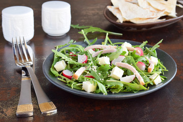 Salad of fresh vegetables - arugula, radish, feta cheese in black plate with flat bread tortilla. Healthy food