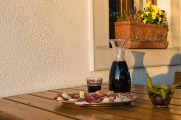 Delicious italian food and drink: red wine accompained by raw ham, salami, cheese and other tasteful cold cuts. All served on a rustic wooden table