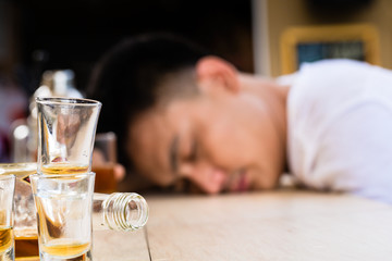 Empty bottle and glasses in front of drunk man