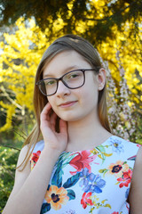 Fototapeta na wymiar Portrait of beautiful girl with glasses and brown hair. Young smiling teneeger in green spring park resting among grass and flowers. Lifestyle people concept