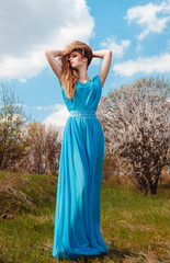 Beautiful girl with long hair in a blue long dress against the sky