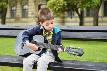 child boy playing on guitar in a park
