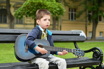 child boy playing on guitar in a park