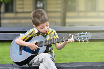 child boy playing on guitar in a park
