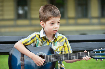 child boy playing on guitar in a park