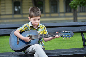 child boy playing on guitar in a park