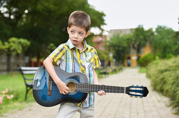 child boy playing on guitar in a park