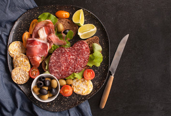 Sandwiches of whole grain bread with ham, bacon, prosciutto, olives and olives with whole grain chips on a black wooden background. Clean food, healthy Breakfast. Top view with copy space