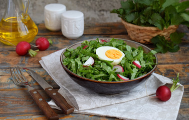 Vitamin salad from lettuce, radish, green onions and eggs, seasoned with vegetable oil in plate on wooden background. Healthy food. Salad of fresh green vegetables