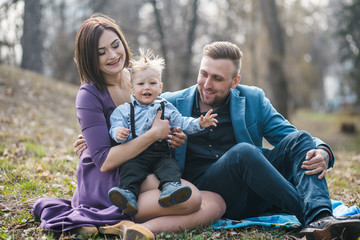 Happy family in the park evening light. The lights of a sun. Mom, dad and baby happy walk at sunset. The concept of a happy family.Parents hold the baby's hands.